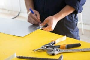 Metalworking technician marking a metal sheet with a blue marker at a yellow workbench.