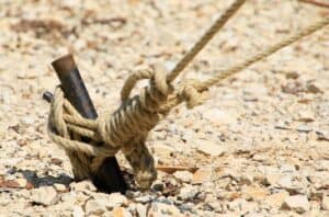 Close-up of a bolt secured with a thick rope tied around it, embedded in rocky ground, demonstrating a makeshift anti-loosening fastening method.