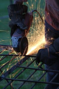 Worker welding steel reinforcement bars with sparks flying, emphasizing industrial metalwork and construction safety.