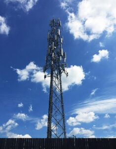 Tall cell tower with multiple antennas and dishes against a bright blue sky with clouds, used for wireless communication and signal transmission.