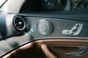Car door interior features a speaker and seat controls.