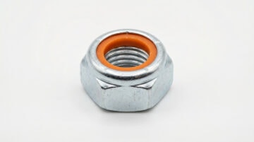 Close-up of a hex nut with an orange insert, used in industrial machinery and construction for secure fastening. High-quality metal nut designed for durability and precision.