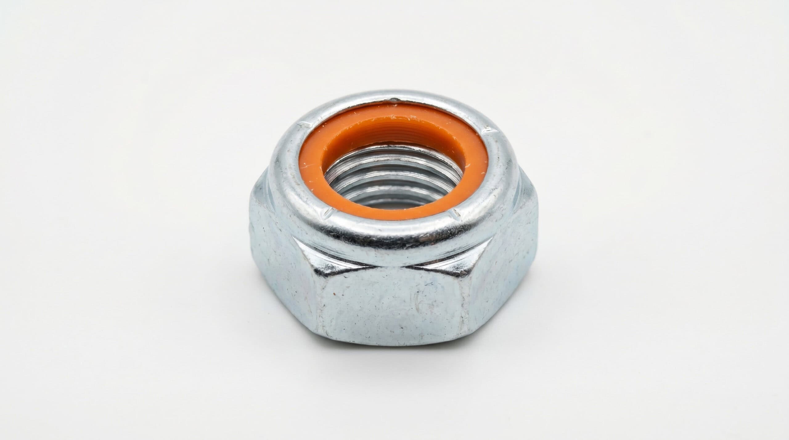 Close-up of a hex nut with an orange insert, used in industrial machinery and construction for secure fastening. High-quality metal nut designed for durability and precision.