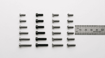 Assorted flange bolts and industrial screws in black, silver, and stainless steel, arranged with a ruler for size reference, showcasing precision manufacturing.